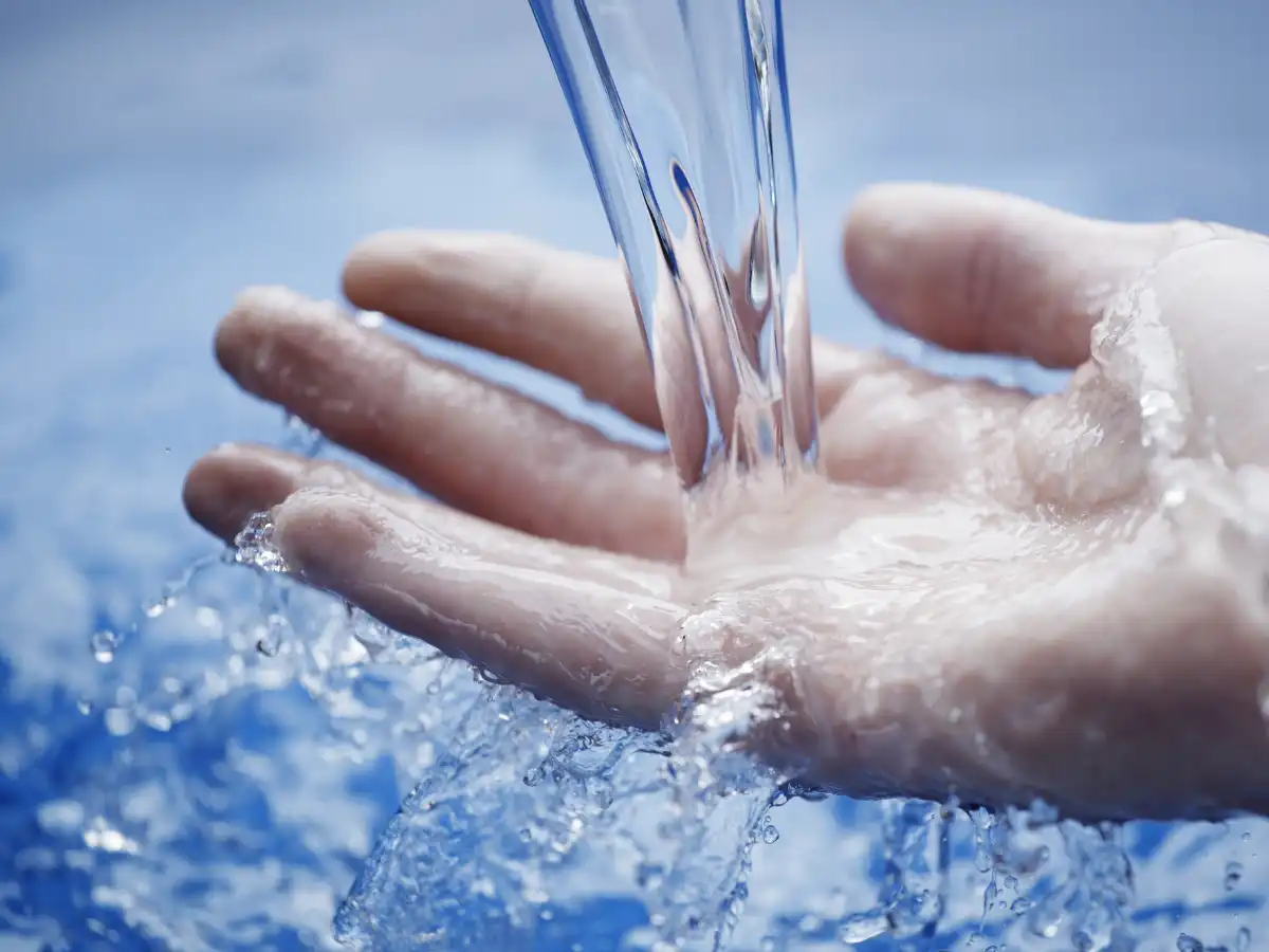 水が流れ落ちて溜まっているところに手のひらに水を当てている画像